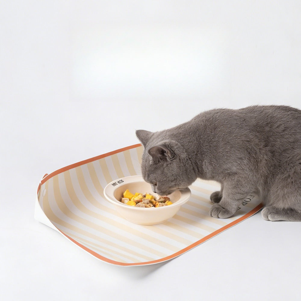 Gray cat eating on a striped pet bowl mat